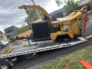 Flatbed tow truck transporting a heavy industrial machine during daytime trade towing service in Melbourne