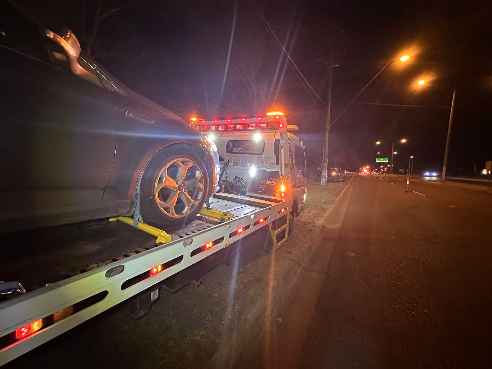 Night time accident towing in Melbourne with a damaged car securely loaded on a flatbed tow truck