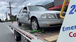 Damaged silver sedan strapped on flatbed after roadside collision