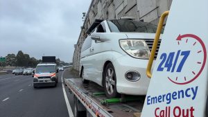 Emergency tow truck transporting a white vehicle on a wet Melbourne freeway