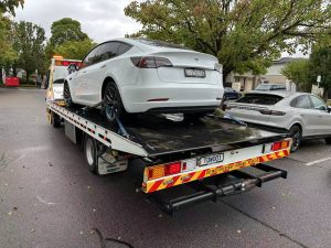 White Tesla Model Y secured on a flatbed tow truck in a Melbourne suburban street