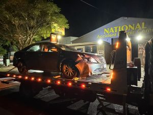 Damaged sedan loaded onto a tow truck outside an accident repair centre in Melbourne at night