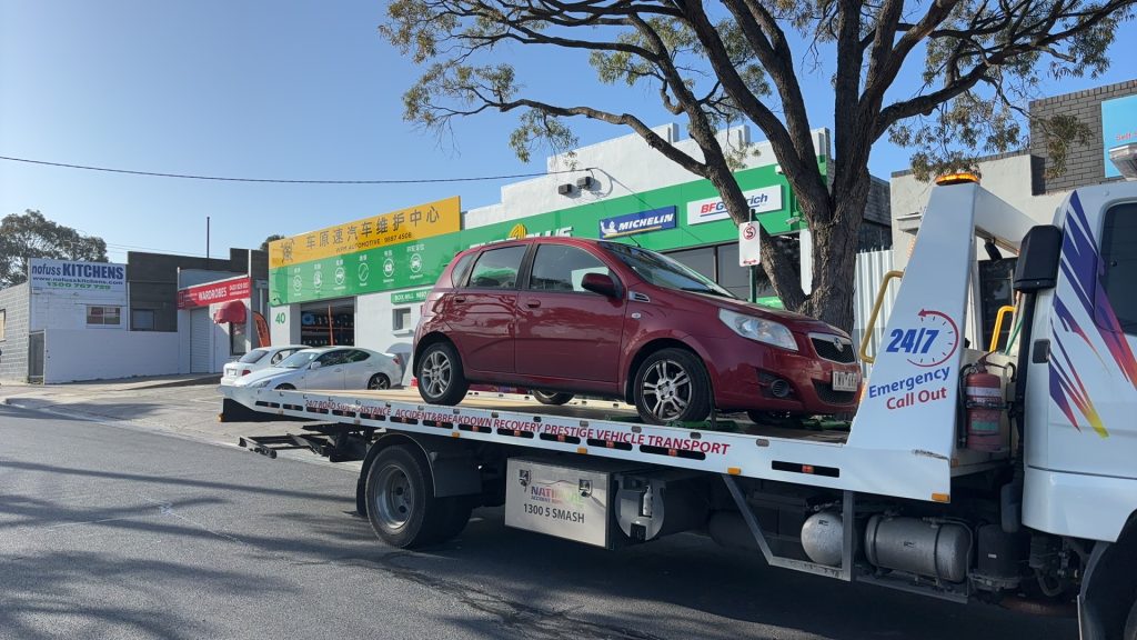 Red hatchback loaded on a flatbed tow truck for affordable towing in Clayton