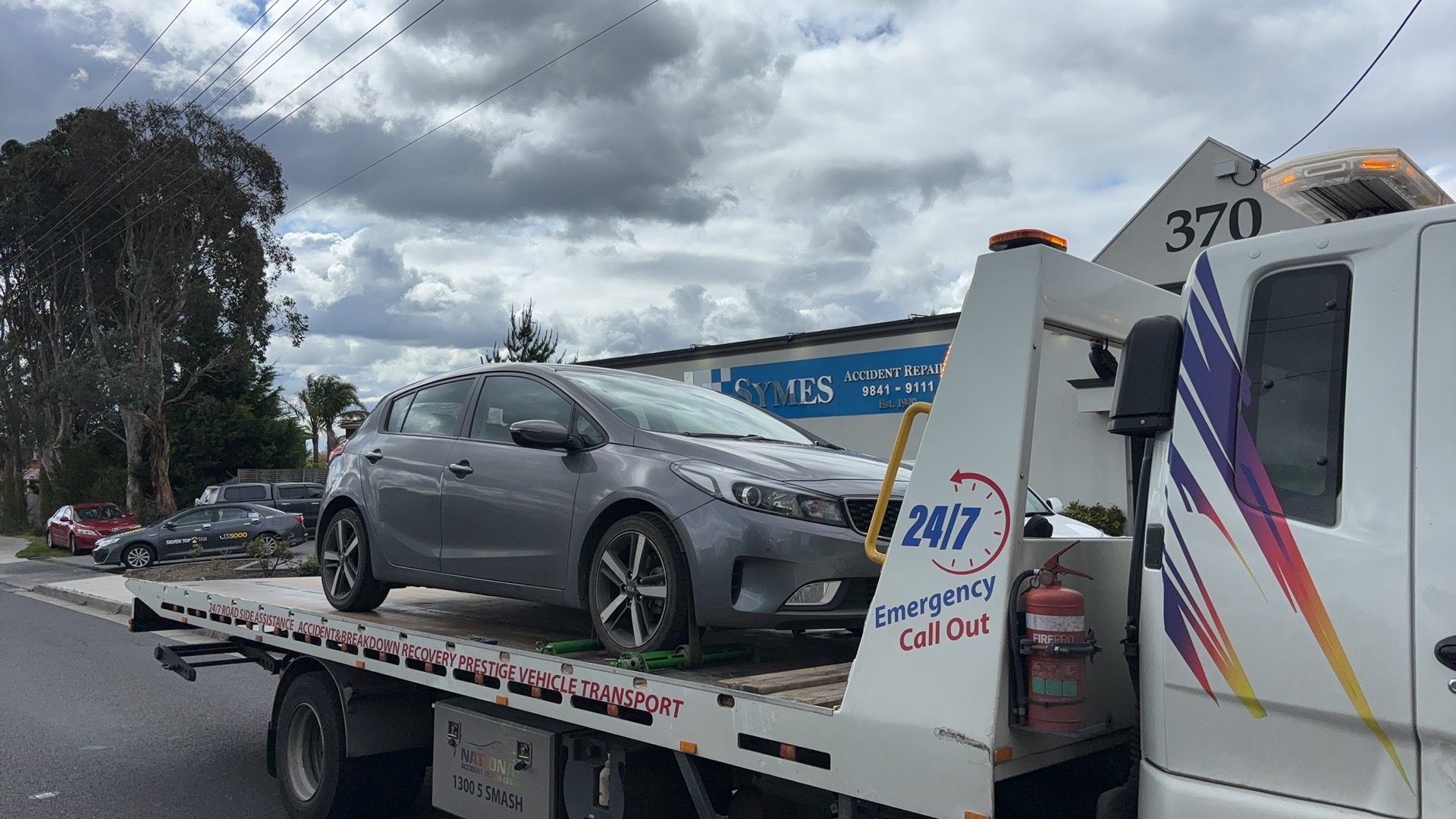 Flatbed tow truck transporting a grey hatchback during a roadside car towing job in Melbourne