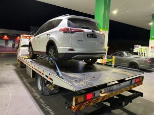 White Toyota RAV4 secured on a flatbed tow truck at a petrol station